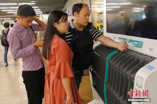 图为没带雨伞的民众在共享雨伞的货架上扫码借用。殷立勤 摄