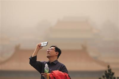 昨日，景山公园，一男士用手机拍摄，身后的故宫在雾霾沙尘下隐隐约约。当天北京沙尘雾霾天气，PM10爆表。新京报记者 王嘉宁 摄