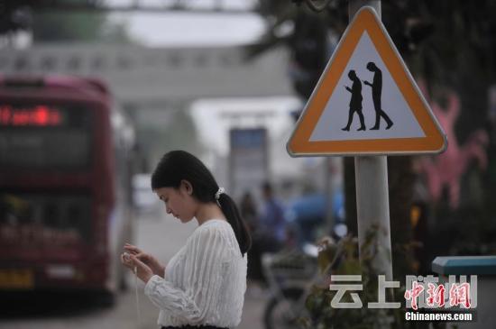 重庆涪陵红酒小镇一红绿灯处摆放了“不做低头族、关注红绿灯”警示牌，提醒市民在过斑马线的时候不能玩手机，注意交通安全。 陈超 摄